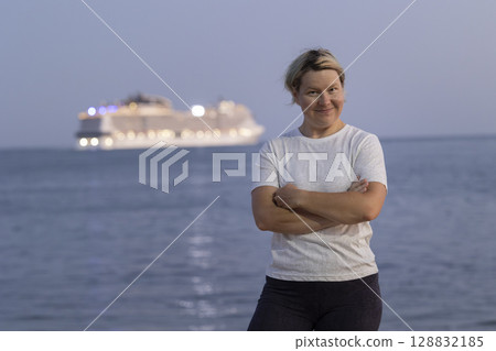 Tourist smiling with arms crossed in front of cruise ship at sunset 128832185