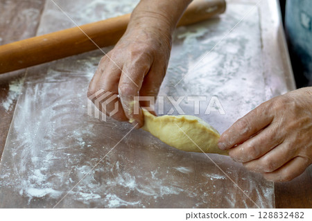 Process of preparing pelmeni on floured surface. Close-up of an elderly woman's hands 128832482