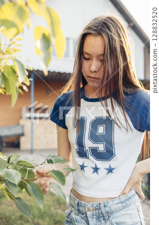 Asian teenage girl in sporty t shirt standing by green tree branches in backyard garden in front of house during sunset in summer concept of natural childhood growth, rural outdoor Asian teenage girl in sporty t shirt standing by green tree branches in backyard garden in front of house during sunset in summer concept of natural childhood growth, rural outdoor 128832520