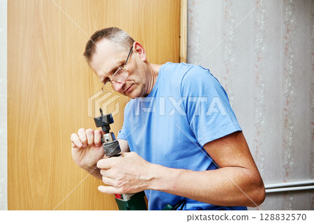 Tightening chuck with chuck key installer prepares hole saw arbor for drilling hole in wooden door during installation of latch assembly. 128832570