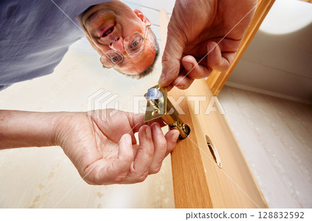 Installing latch mechanism into door edge captured from low angle showing process of inserting rectangular faceplate into predrilled mortise hole. 128832592