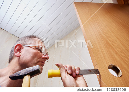 Carving mortise in wooden door, repairman uses chisel and hammer to carefully shape hole for lock installation during door hardware fitting process. Carving mortise in wooden door, repairman uses chisel and hammer to carefully shape hole for lock installation during door hardware fitting process. 128832606