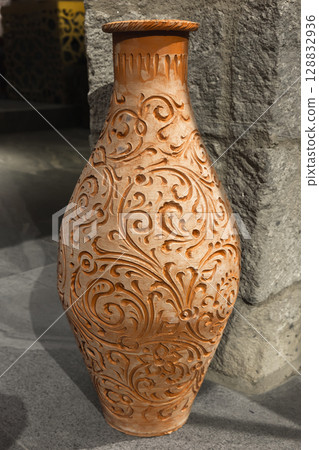 Ornate Clay Vase Featuring Intricate Floral Engraving Against a Stone Background 128832936