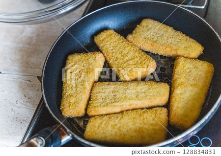 Breaded fish fillets frying in a pan on the stove 128834831