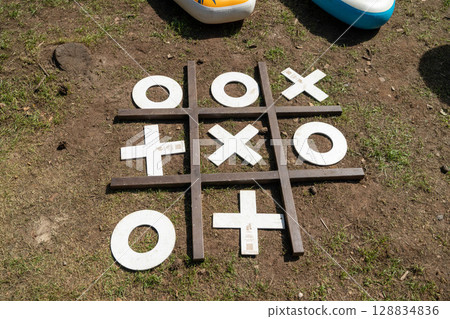 Giant tic-tac-toe game set up on grass outdoors with inflatable boats in background 128834836