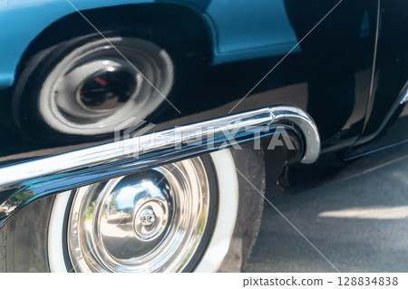 Shiny chrome details and whitewall tire of a classic car reflecting another car's wheel 128834838