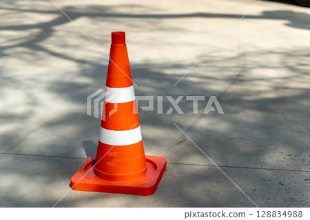 Bright orange traffic cone standing on concrete surface 128834988