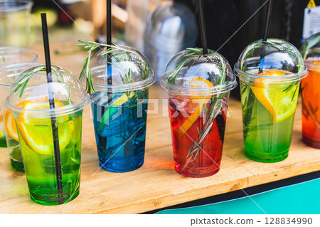 Colorful cocktails with straws and rosemary on wooden table 128834990