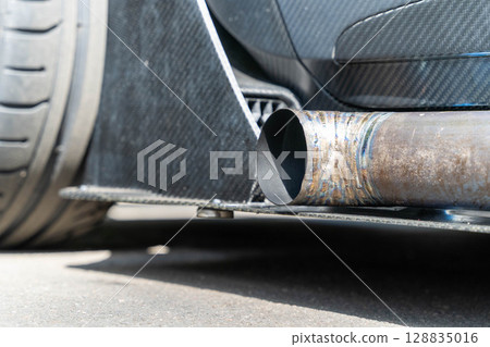 Large exhaust pipe protruding from carbon fiber undercarriage of sports car 128835016