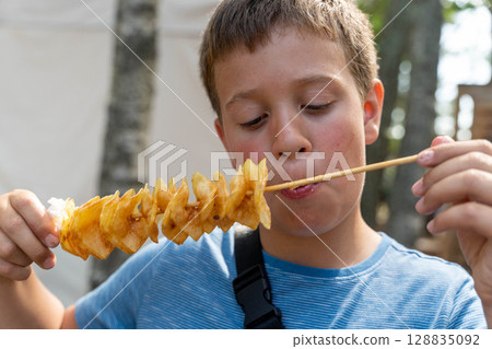 Boy eating tornado potato on a stick at summer festival 128835092