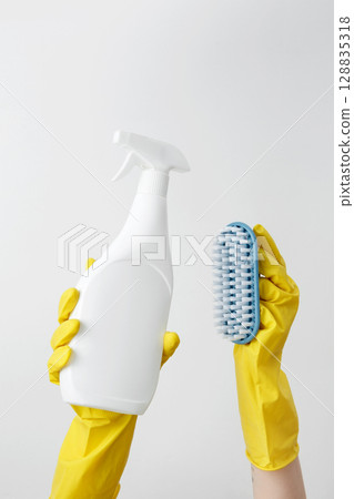 Woman in rubber gloves holding cleaning spray and brush, ready for household cleaning tasks 128835318