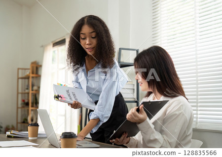 Collaborative Work. Two women reviewing documents in a modern office setting. 128835566