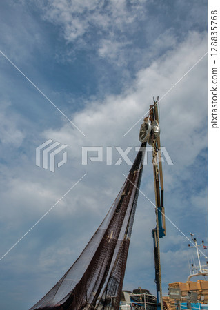 Fishing net hanging from boat mast against sky 128835768