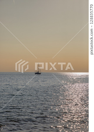 Sailboat silhouette on calm sea at golden hour sunset 128835770