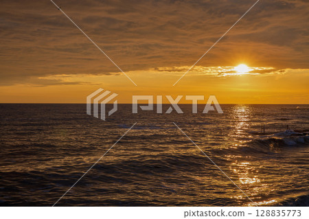 Golden sunset over calm ocean with pier silhouette Golden sunset over calm ocean with pier silhouette 128835773