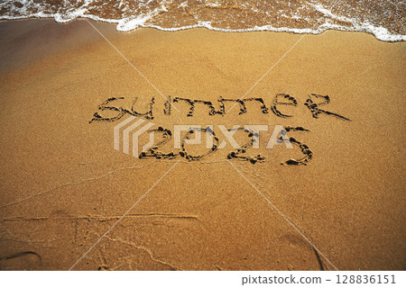 Hand drawn message Summer 2025 on wet yellow sand on beach of sea 128836151