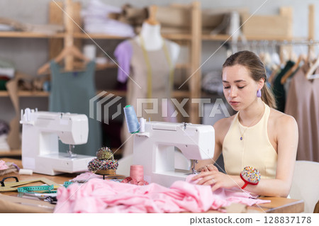 Seamstress working on modern sewing machine in sewing workshop Seamstress working on modern sewing machine in sewing workshop 128837178