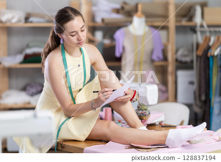 Girl sitting on table drawing sketches on white sheets 128837194