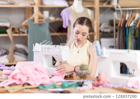 Woman seamstress sews on sewing machine in workshop 128837200