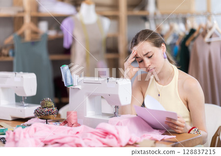 Upset female dressmaker checking some documents in tailor shop 128837215