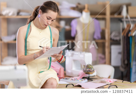 Young woman seamstress draws sketch sitting on table 128837411