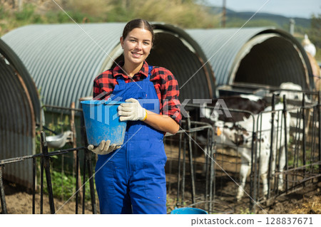 Young woman with bucket at pen with calves 128837671
