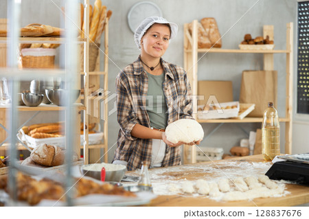Working in bakery - girl kneads raw dough to make baguettes or croissants 128837676