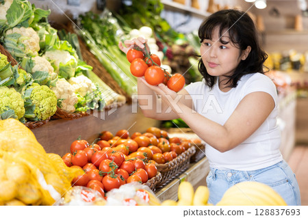 Young asian girl selecting ripe red tomatoes in supermarket 128837693