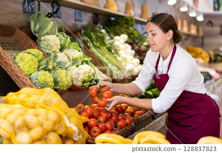 Young female seller laying out tomatoes on display in store Young female seller laying out tomatoes on display in store 128837823
