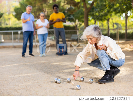 Multiracial mature adult people measuring distance between balls in petanque game outside in a park Multiracial mature adult people measuring distance between balls in petanque game outside in a park 128837824