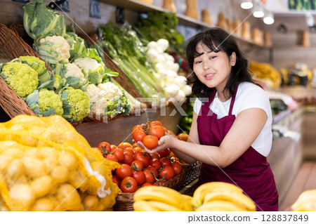 Young asian salesgirl offering ripe tomatoes in greengrocery 128837849