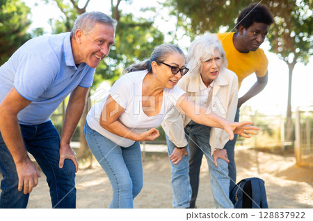 Carefree multiracial friends throwing metal balls on a sandy background in the park 128837922