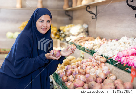 Portrait of female customer in paranja selecting onion in supermarket 128837994