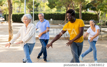 Happy seniors and middle-aged people exercising together dance in a sunny park 128838012