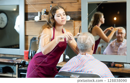 Young female barber making haircut to elderly client in barbershop Young female barber making haircut to elderly client in barbershop 128838090