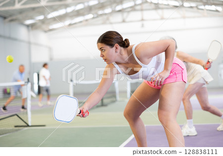Young woman bouncing ball in pickleball game on court with racket Young woman bouncing ball in pickleball game on court with racket 128838111