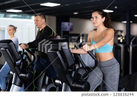 Athletic young woman exercising on an elliptical trainer in gym 128838244