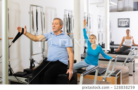 Two female and male training back while working out on Pilates reformer machine bed in studio. Wellbeing and healthy lifestyle concept 128838259