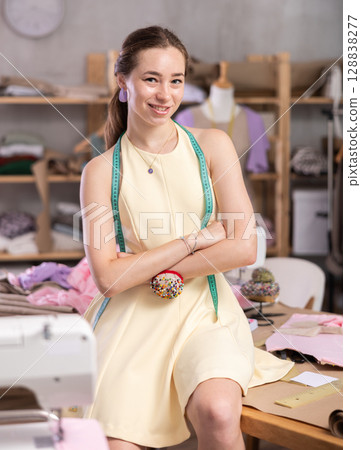 Young woman sitting on table in sewing workshop Young woman sitting on table in sewing workshop 128838277