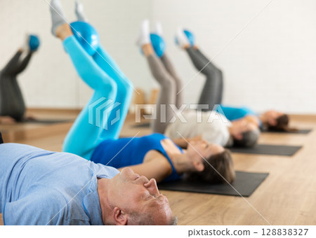Group of young elderly people in sportswear exercising Pilates with mini balls while lying on mats in rehabilitation center 128838327