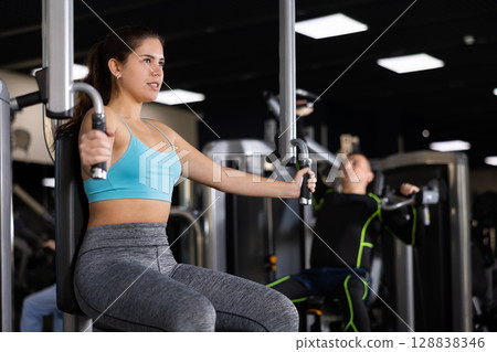 Young girl performing chest exercises in butterfly machine 128838346