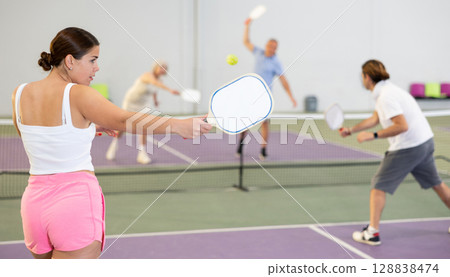 Rear view of girl with white racket playing pickleball tennis 128838474