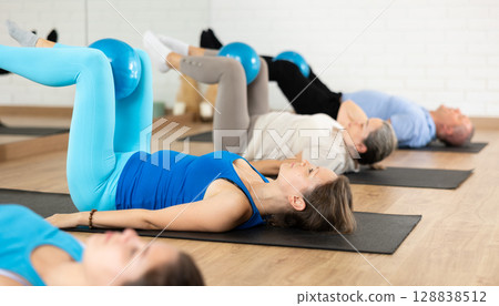 Woman exercising with bender ball during group training at gym. 128838512