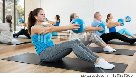 Young woman practicing pilates with ball in gym area 128838560