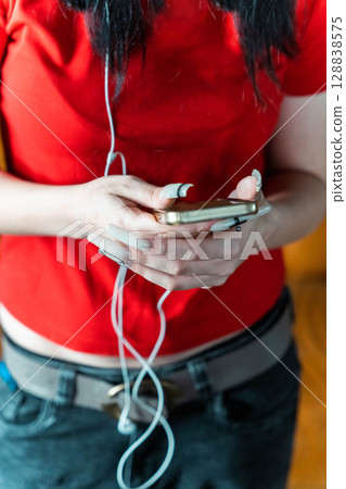 Young woman using smartphone and listening music with earphones 128838575