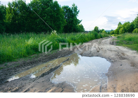 Large puddle blocking dirt road in green rural landscape Large puddle blocking dirt road in green rural landscape 128838690