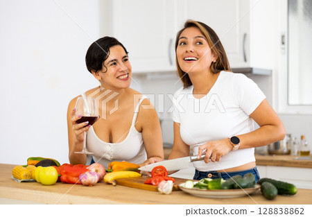 Smiling Hispanic women drinking wine and cooking in home kitchen Smiling Hispanic women drinking wine and cooking in home kitchen 128838862