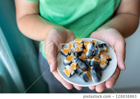 Child holding small plate of gummy candy in open hands Child holding small plate of gummy candy in open hands 128838863