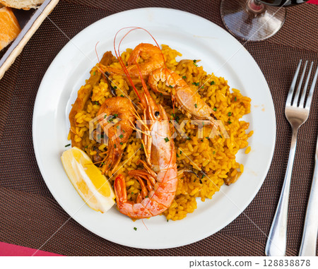 Paella made of rice and different seafood served in plate with table appointments 128838878