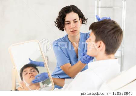 Beautician woman using mirror consulting man in clinic 128838943